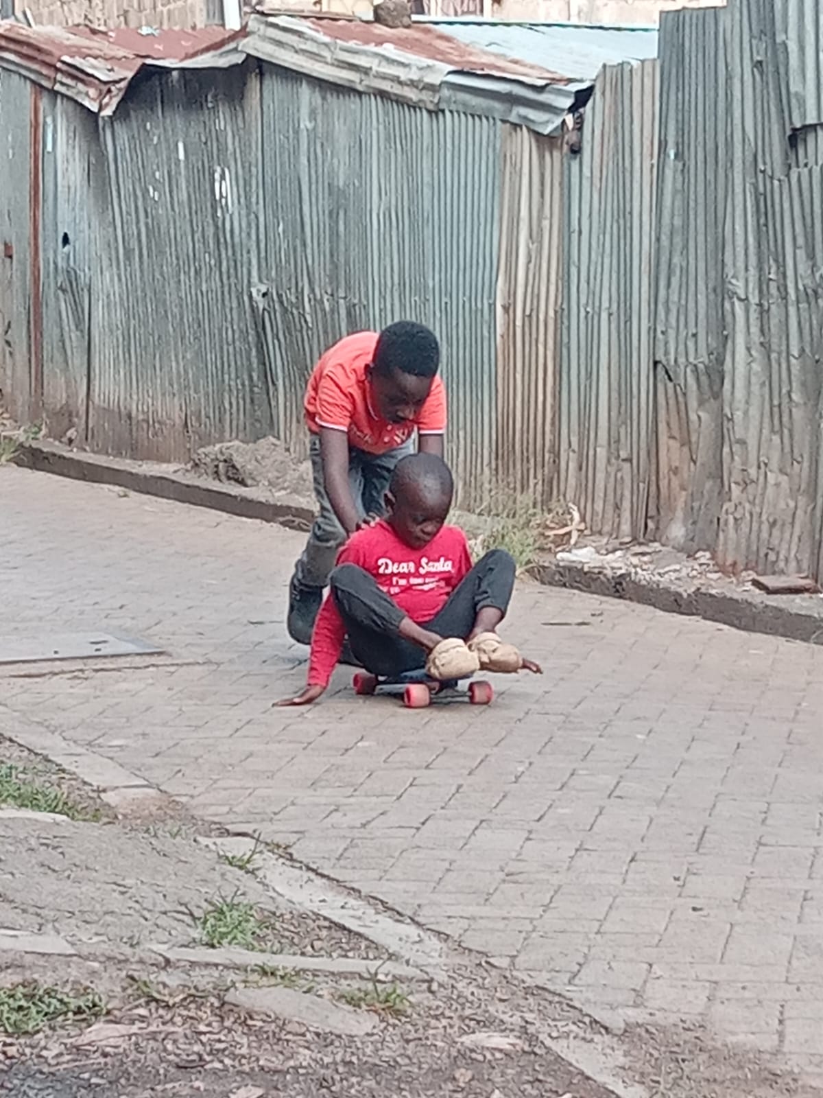 Teen mentor guiding a young child on a skateboard in Kibera