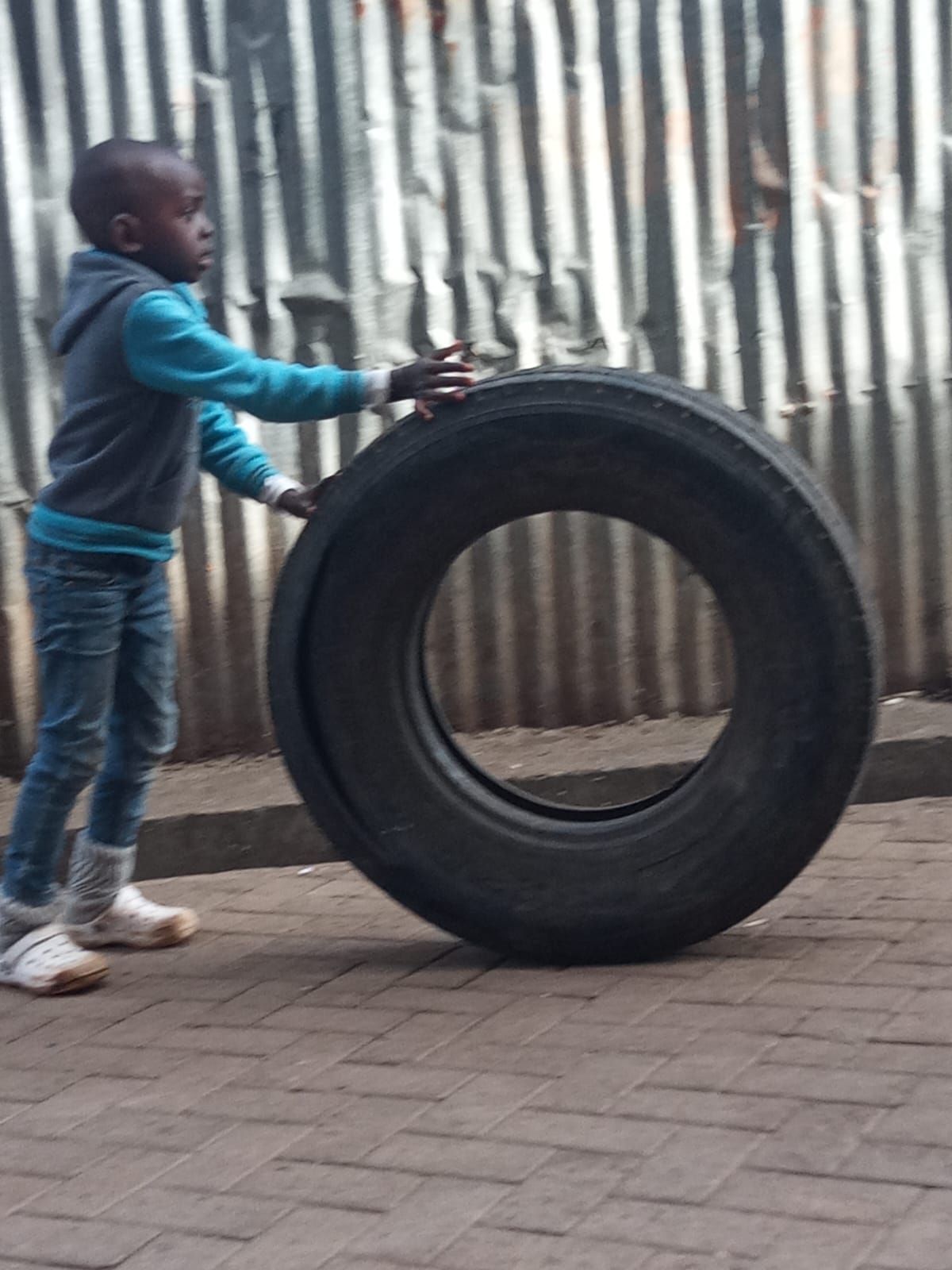 Child rolling a tyre down a Kibera street — pure childhood joy